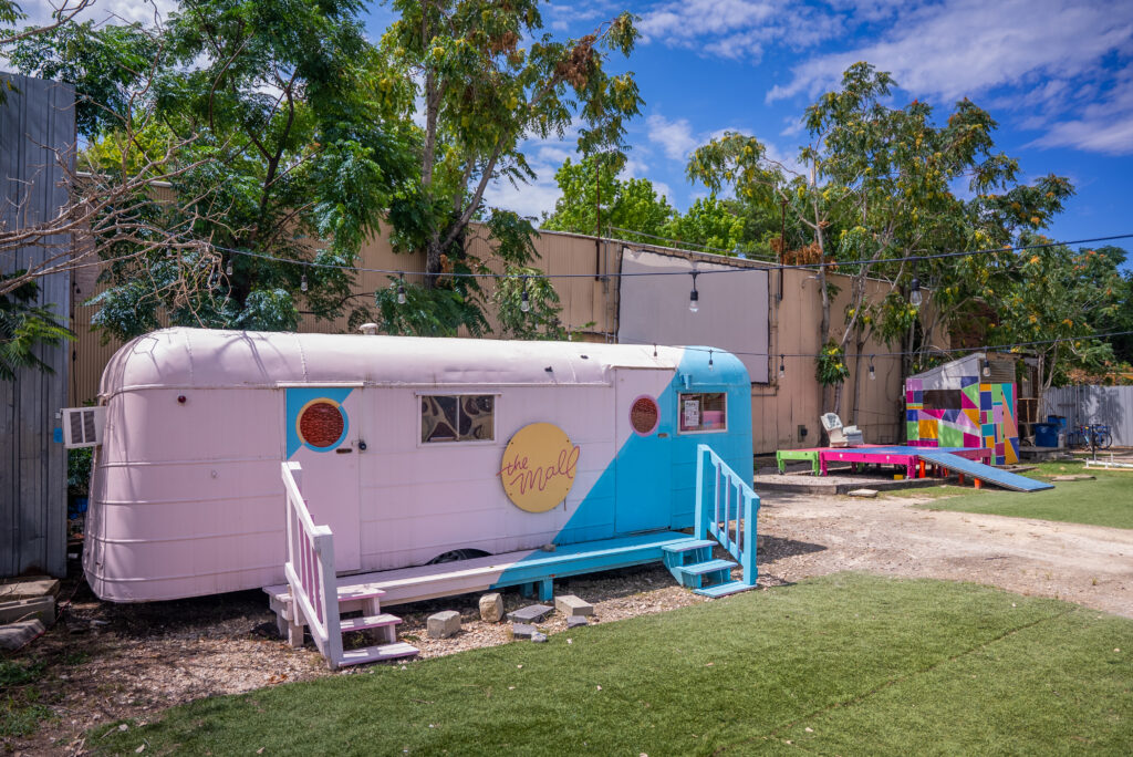 an airstream trailer is painted with pink and turquoise, positioned in front of the Museum of Human Achievement entrance.